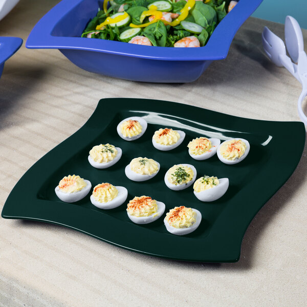 A Tablecraft hunter green cast aluminum platter with deviled eggs and salad on a table.