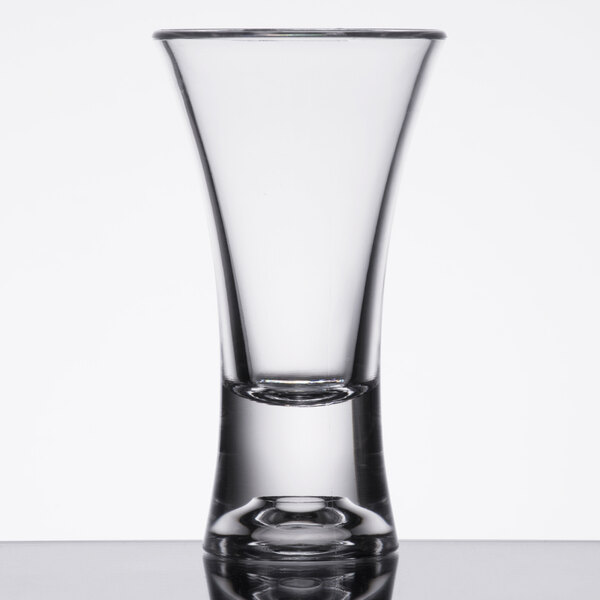 A close-up of a Thunder Group clear plastic flared shot glass on a table with a reflection.