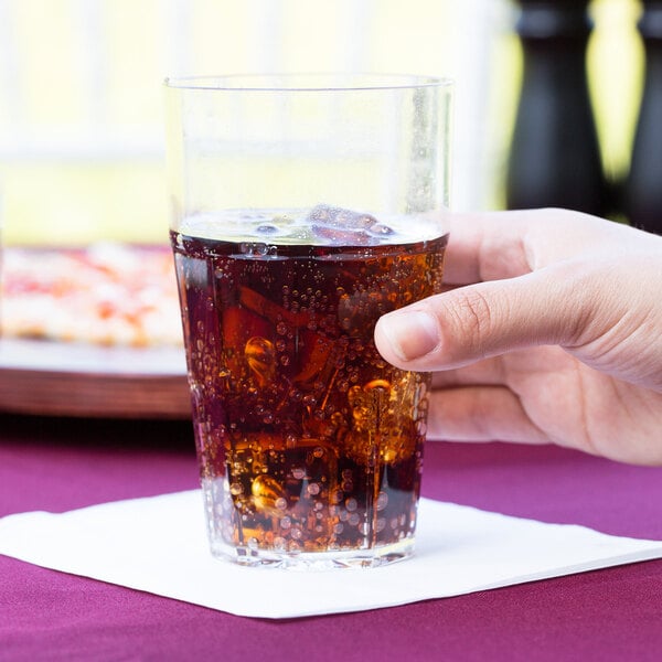 A person holding a Thunder Group clear plastic tumbler of brown soda at a table with pizza.