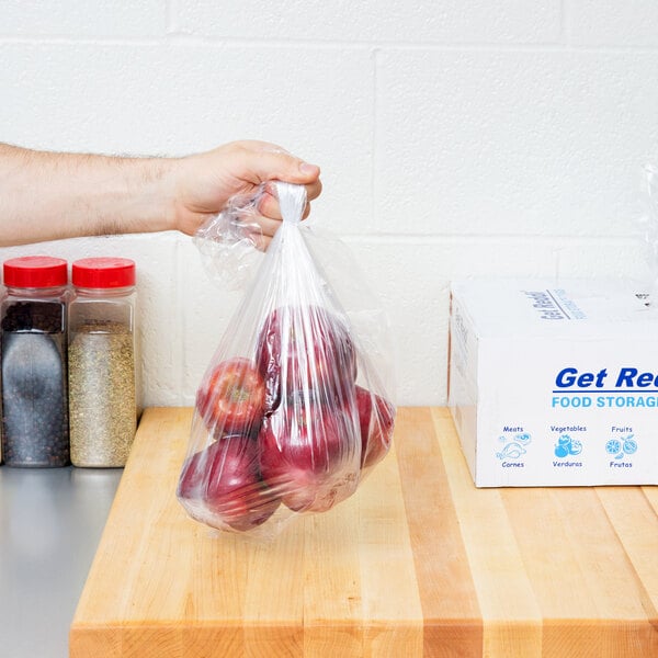 A hand holding a plastic bag of red apples.