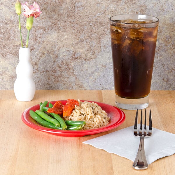 A red Sensation wide rim melamine plate with rice and vegetables on a table.