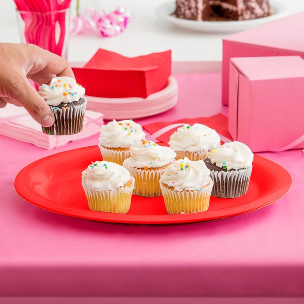 A hand holding a cupcake on a red oval platter.