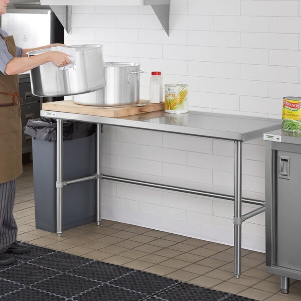 A woman in an apron using a Regency stainless steel open base work table in a kitchen.