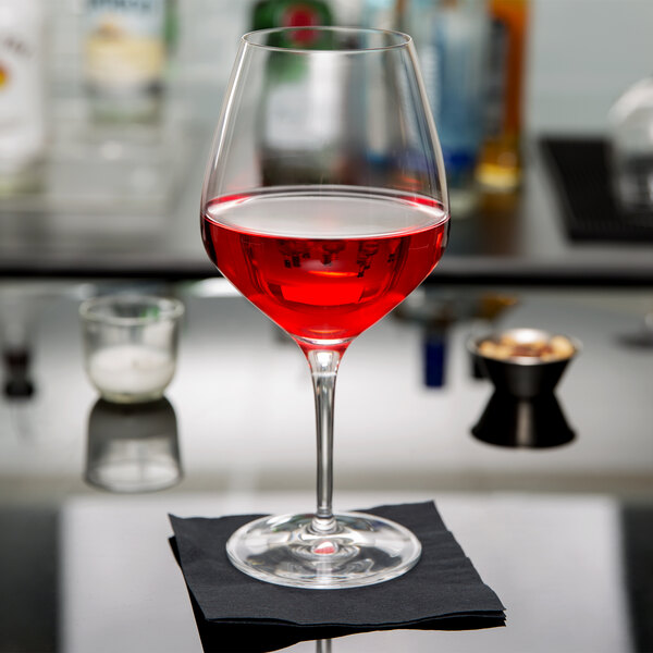 A Spiegelau Authentis Burgundy wine glass filled with red wine on a black napkin.