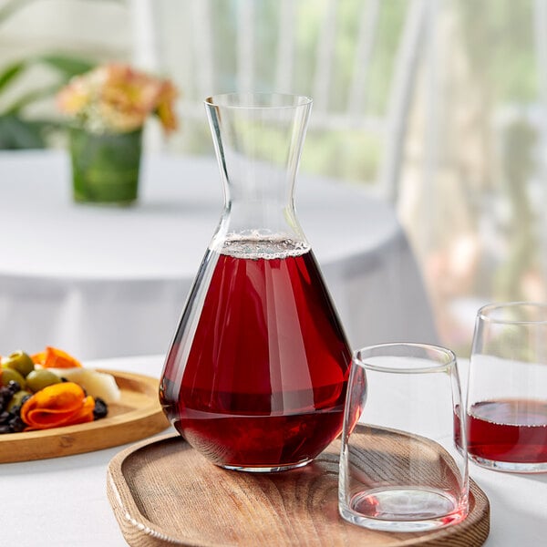 A Spiegelau glass decanter with red liquid on a table.