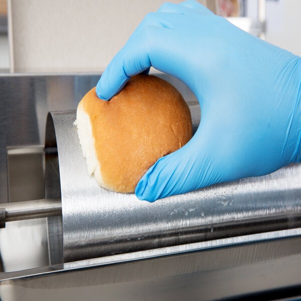 A person in blue gloves using an APW Wyott vertical conveyor bun grill toaster to toast a roll.