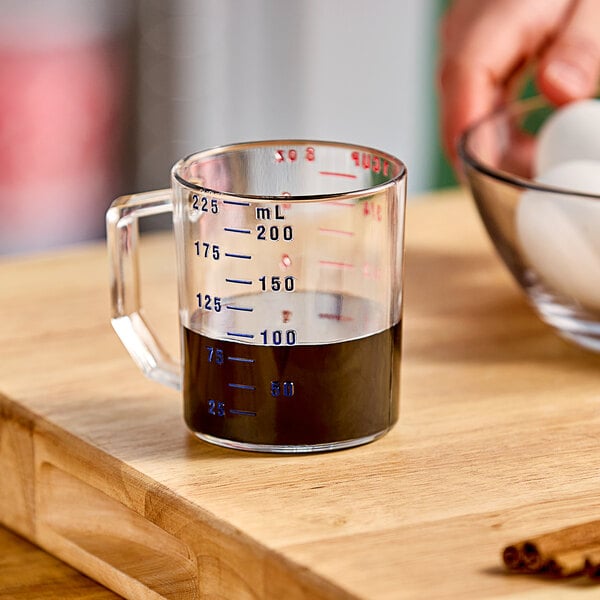 A hand using a Cambro clear polycarbonate measuring cup to measure dark liquid.