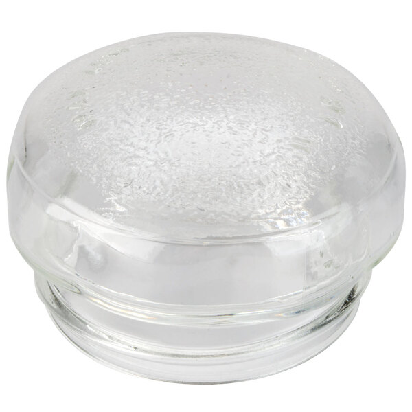 A clear glass container with a round top over a close-up of a white surface.