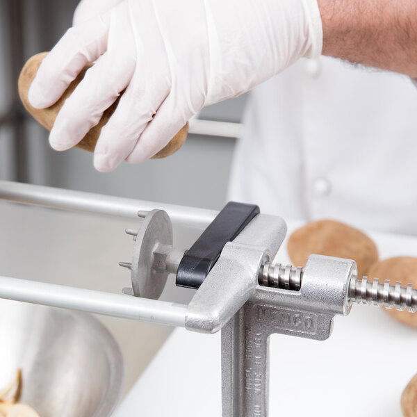 A gloved hand using a Nemco support rod to cut potatoes.