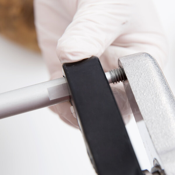 A person in white gloves using a metal support rod to attach a metal pipe.