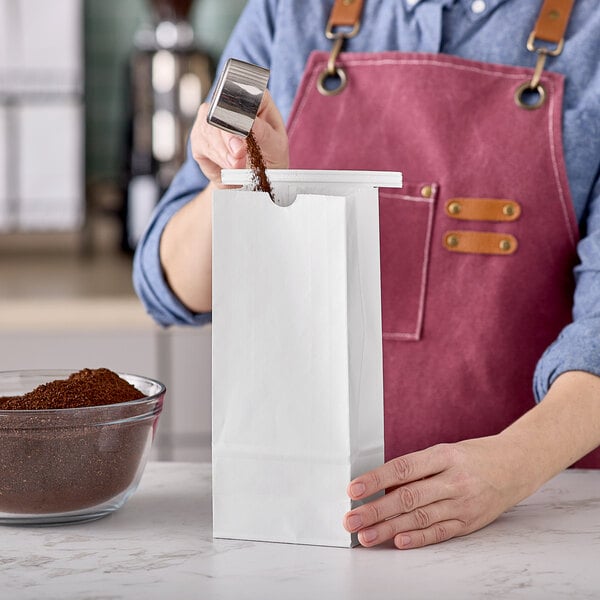 A person pouring coffee into a white paper bag with a silver tin tie.