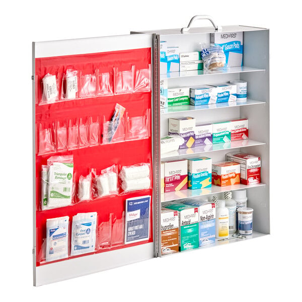 An open metal cabinet with five shelves and a door, containing various first aid supplies organized in boxes and clear pockets.