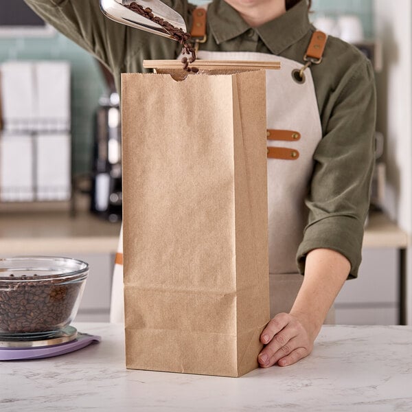 A woman pouring coffee into a brown paper bag on a white surface.