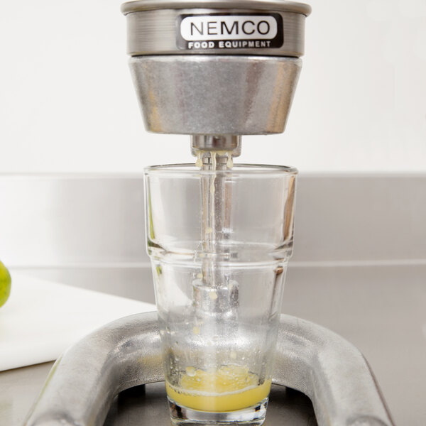 A Nemco Easy Citrus Juicer cone attached to a glass of juice being poured into a metal pipe.