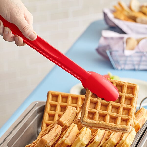 A person using a red Cambro scallop grip tong to hold a waffle.