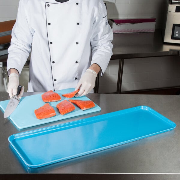 A chef cutting salmon on a blue market tray.