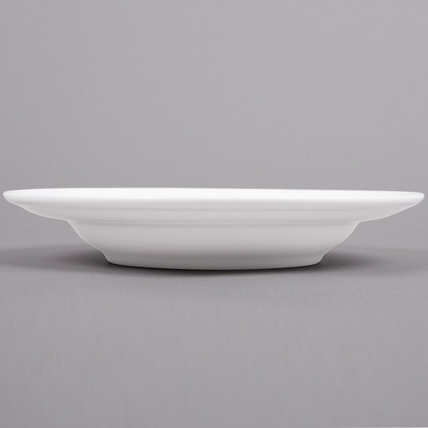 An Arcoroc white soup plate with a rim on a gray surface.
