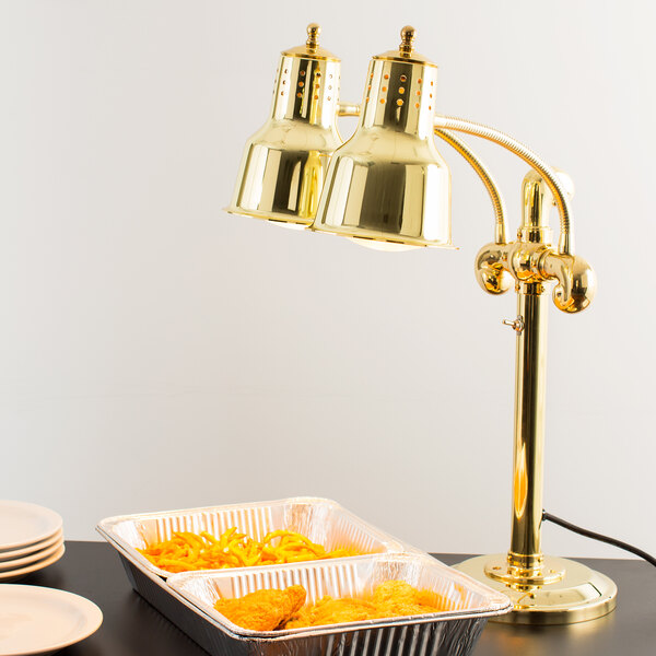 A Hanson Heat Lamps brass freestanding heat lamp with dual bulbs over a table with food in a tray.