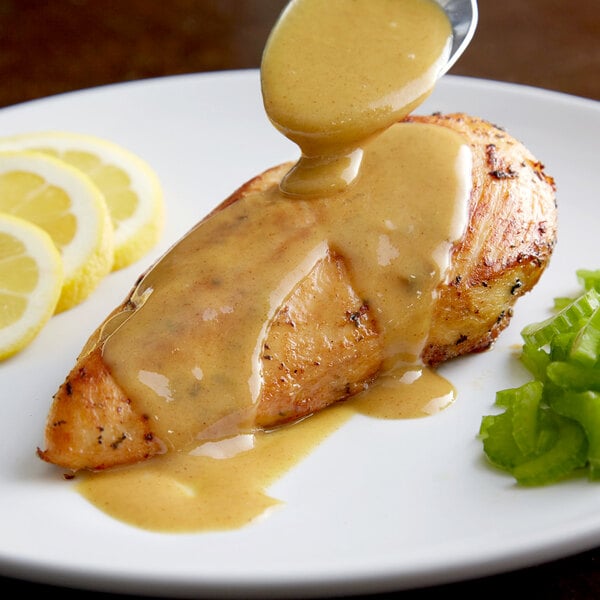A plate of chicken with yellow mustard sauce and a lemon slice.