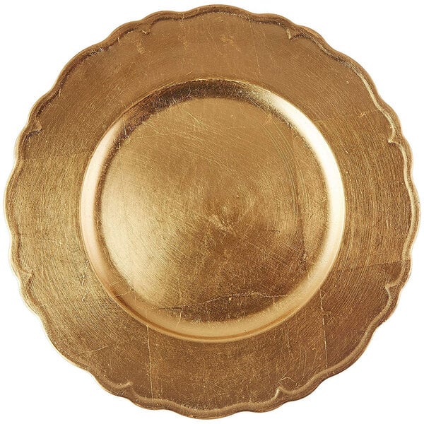 A close up of a gold Charge It by Jay plastic charger plate with a scalloped edge.