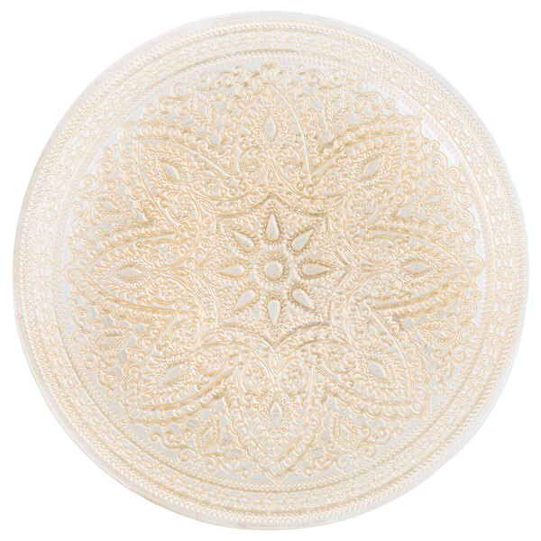 A round gold glass charger plate with an intricate design.