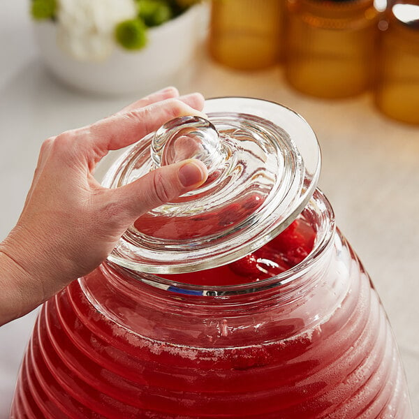 A person using a Replacement Lid for an Acopa glass beverage dispenser to pour red liquid into a glass jar.