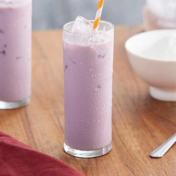 A glass of Big Train Dragonfly Taro Frappe Mix with a straw in it filled with purple liquid and ice.