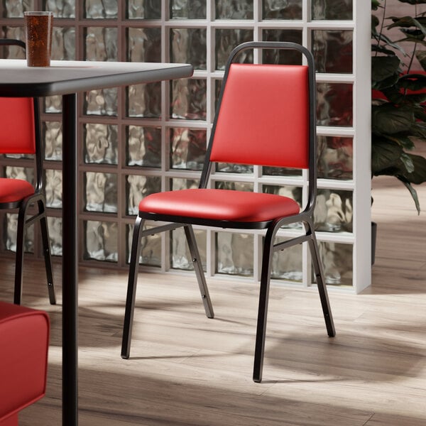 A red Lancaster Table & Seating banquet chair with a padded seat on a table in a restaurant dining area.