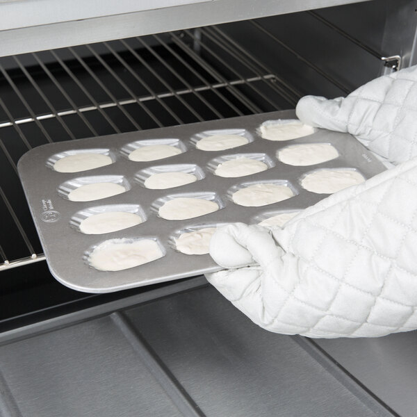 A person in white gloves using a Chicago Metallic Madeleine Pan.