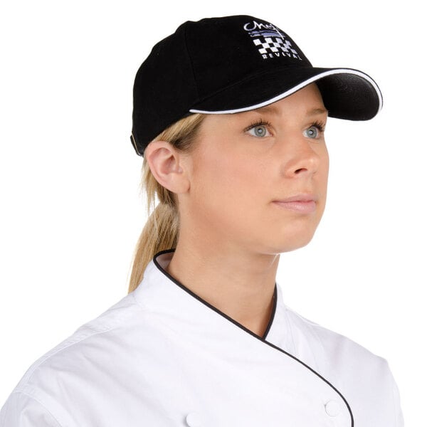 A chef wearing a black Chef Revival baseball cap with a white logo.