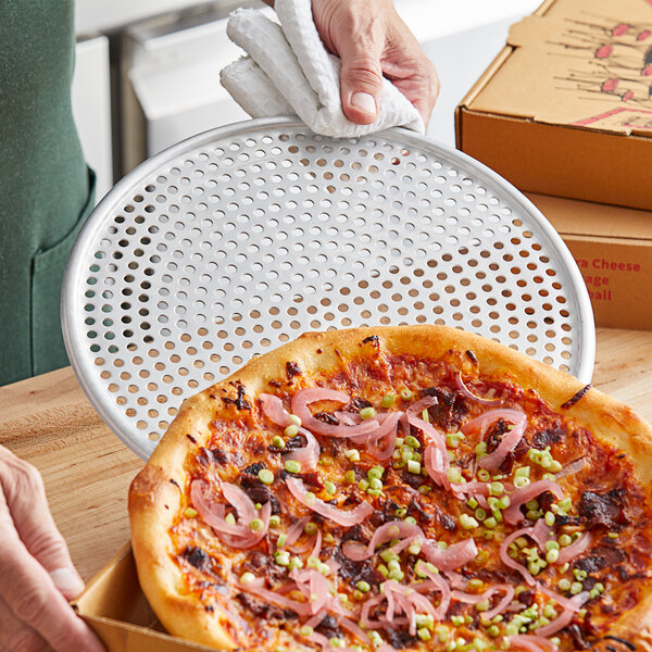 A hand using an American Metalcraft 11" perforated pizza screen to hold a pizza.