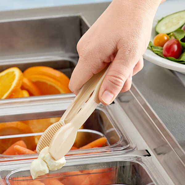 A hand using a beige plastic tong to serve food from a container.