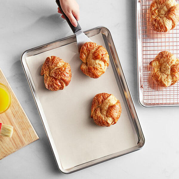 A hand using a spatula to cut croissants on a Baker's Mark PanPal liner.