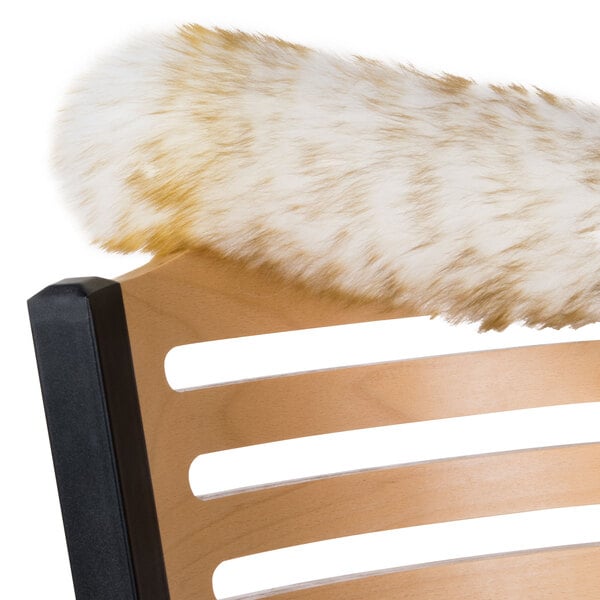 A furry white and brown lambs wool duster on a wooden chair with a furry tail.