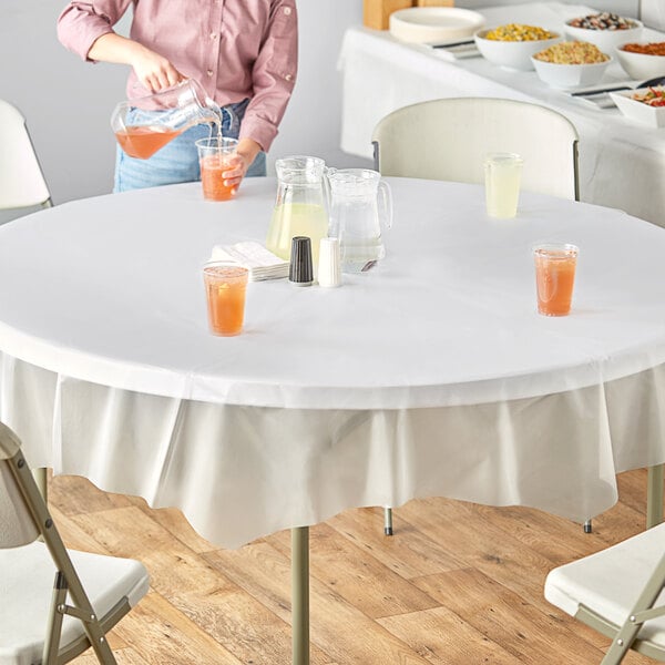 A woman pouring drinks onto a table set with Creative Converting clear plastic table covers and glasses of liquid.