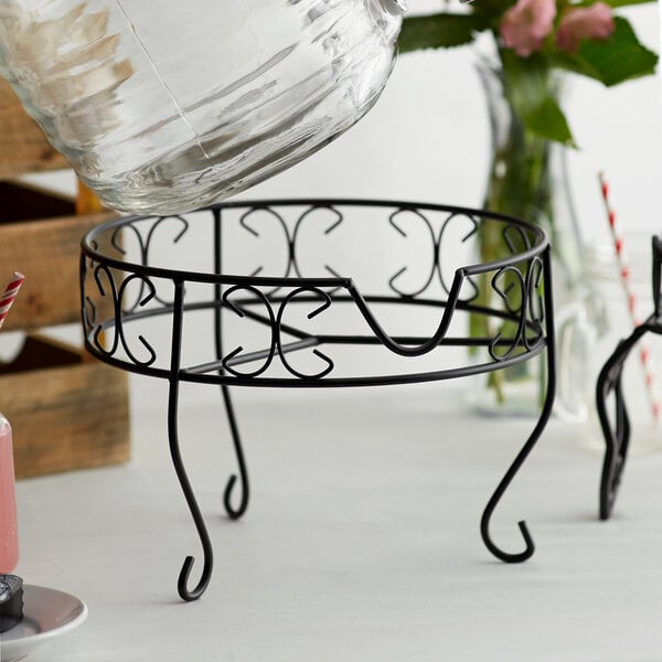 A Metal Stand for an Acopa Beverage Dispenser on a table with a glass bowl on it.