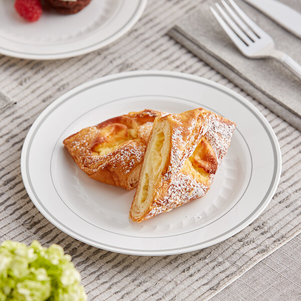 A WNA Comet white plastic plate with silver accent bands holding pastries with a fork on it.