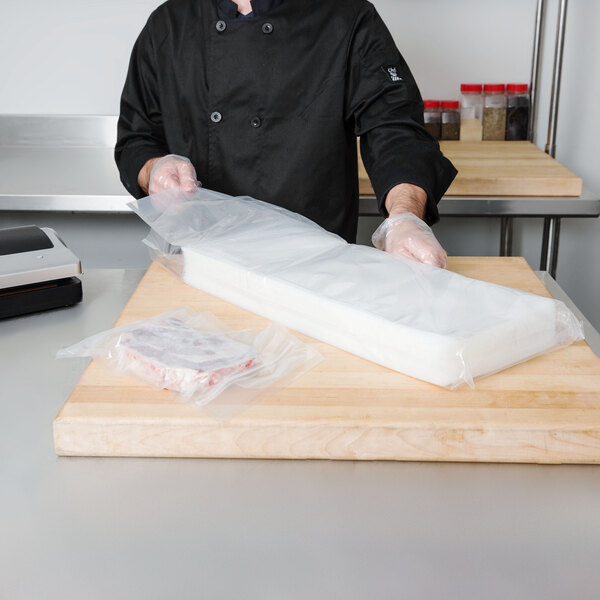 A person wearing gloves holding an ARY VacMaster chamber vacuum packaging bag of food.