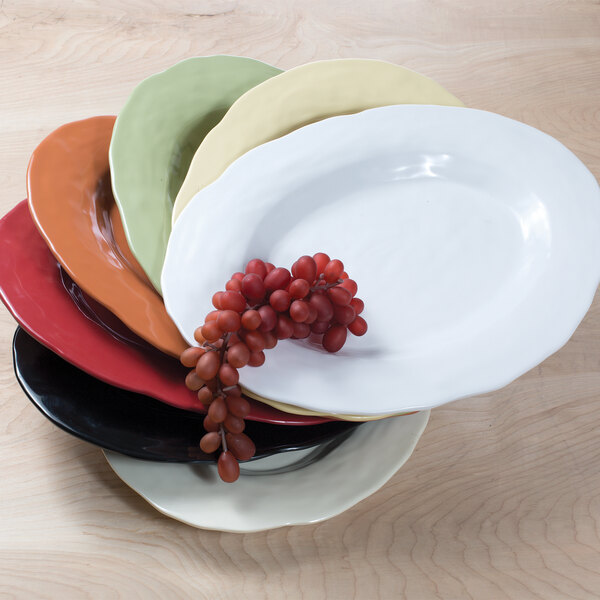 An Elite Global Solutions Tuscany white oval melamine platter with grapes on it in a stack of plates.