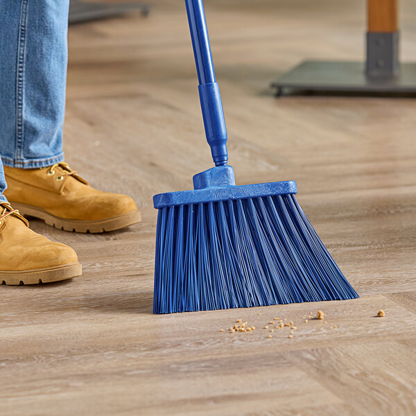 A person using a Carlisle blue broom with unflagged bristles to sweep a floor.