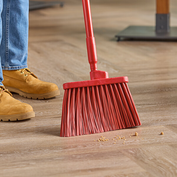 A person sweeping the floor with a red Carlisle broom.