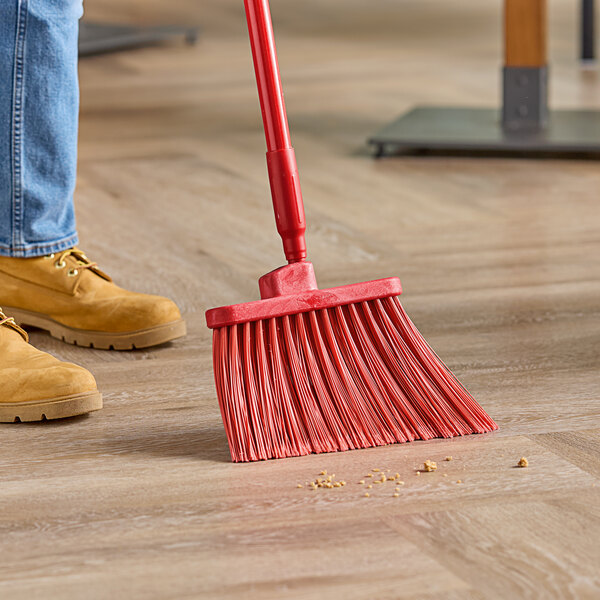 A person sweeping the floor with a red Carlisle angled broom head.
