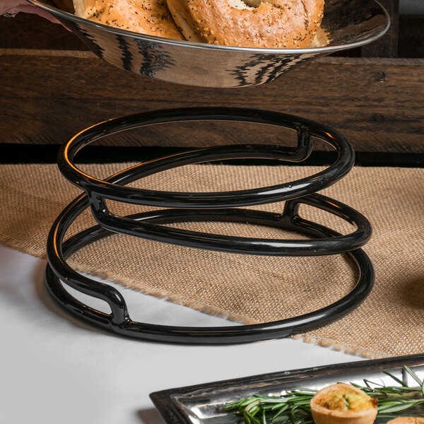 A bagel on a metal stand with brown bread on a table.