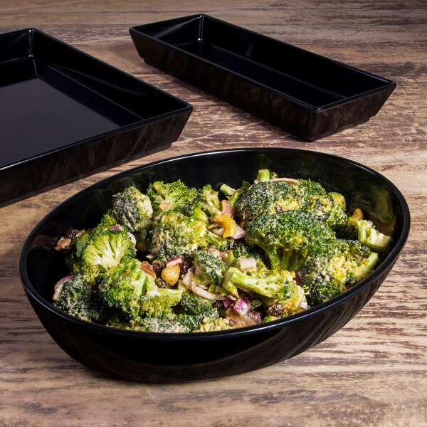 A black oval melamine bowl with broccoli on a table in a salad bar.