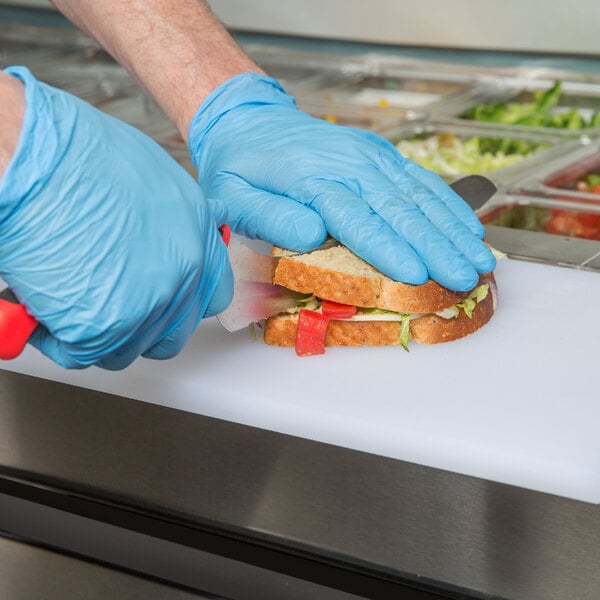 A person wearing blue gloves cutting a sandwich on a counter with an Arctic Air 2 Door Mega Top Refrigerated Sandwich Prep Table.