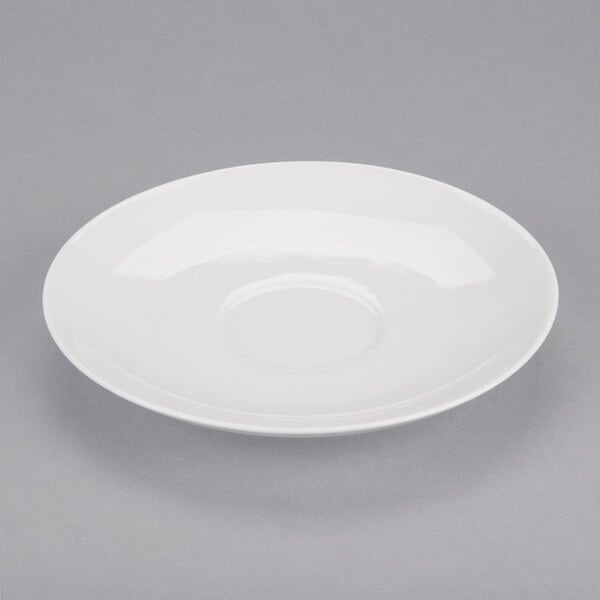 A white porcelain saucer with a round center on a gray surface.