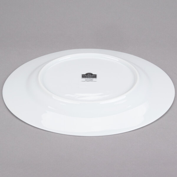 A white 10 Strawberry Street porcelain charger plate with a black rim on a gray surface.