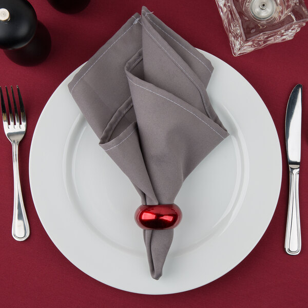 A white 10 Strawberry Street porcelain charger plate with silverware and a red napkin on a table.