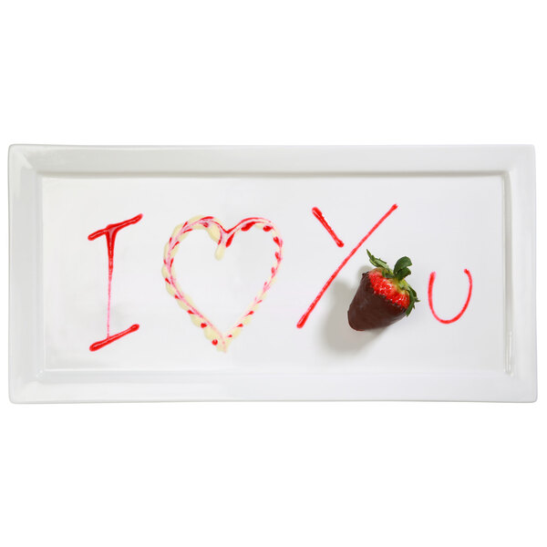 A white plate with a heart drawn in red icing and a strawberry on it.