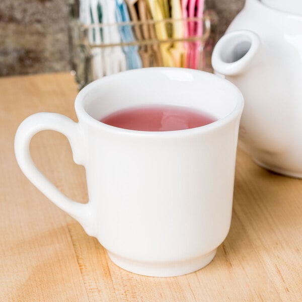 A Homer Laughlin bright white china tea cup filled with tea on a wooden table.